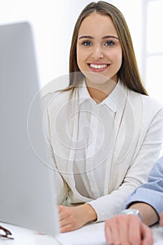 Business woman and man sitting and working with computer in office. Colleagues discussing something at meeting