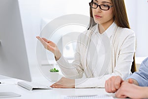 Business woman and man sitting and working with computer in office. Colleagues discussing something at meeting