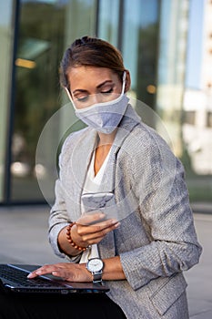 Business woman with mask working on laptop and mobile phone