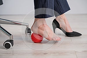 Business woman massages her feet on a massage ball with spikes.