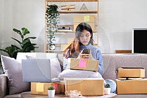 Business woman owner holding parcel box for delivery and using smartphone at home office. Entrepreneur small business working at