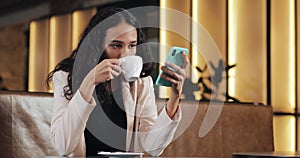 Business woman in pink suit using smartphone and drinking coffee in cozy cafe