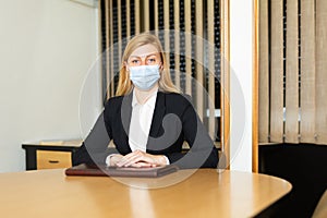 Business woman in protective mask sitting in her office at the negotiating table