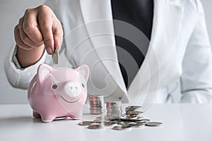 Business woman putting coin into pink piggy bank for planning step up growing business to profit and saving with piggy bank,