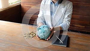 A business woman is putting the coins in a blue piggy bank , saving money is an investment for the future. Banking investment