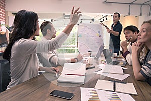 Business woman raise hand for ask question to businessman who is standing and explaining chart in front of meeting room, concept f