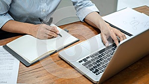 Business woman reading business report to checking financial data on laptop and writing information on document