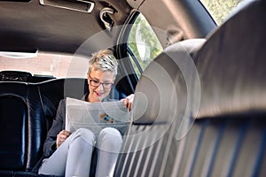 Business woman reading newspaper in limo