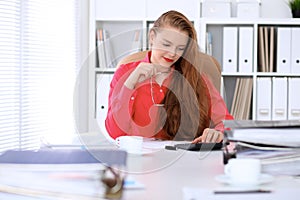 Business woman in red blouse making report, calculating or checking balance.