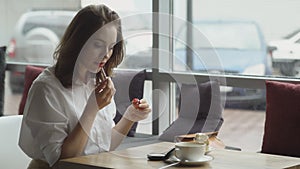 Business woman refreshing make-up after lunch break in cafe. girl paints lips