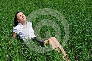 Business woman relaxing in green grass field outdoor under sun. Beautiful young girl dressed in suit resting, spring landscape, br