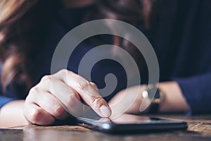 A business woman`s hand touching and sliding finger on a black smart phone on wooden table