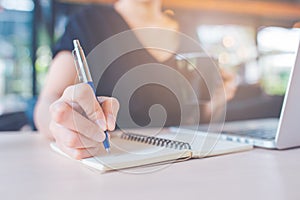 Business woman`s hand is writing on a notebook with a pen