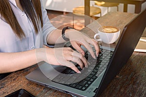 Business woman`s hands working and typing on laptop keyboard on wooden table