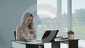 Business woman scrolling mobile at work place. Smiling lady having break.