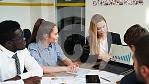 Business woman shows presentation with charts, diagrams on laptop for multiethnic partners. Startup team discuss project
