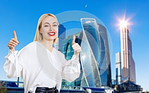 Business woman shows thumbs up gesture over cityscape background.