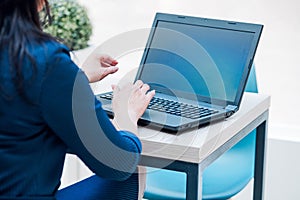 Business woman sits with her back to the camera and types on something on a laptop.