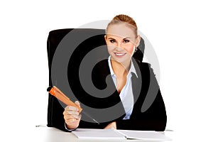 Business woman sitting behind the desk and writes something with big pen