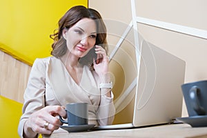 Business woman is sitting in cafe in front of laptop screen and talking on a cell phone