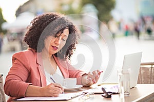 Business woman sitting in cafÃ© using laptop and writing on document