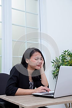 Business woman sitting on chair while closing her eyes in front of laptop