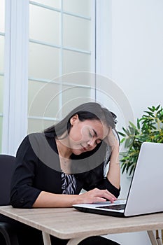 Business woman sitting on a chair while closing her eyes and holding her head in front of a laptop