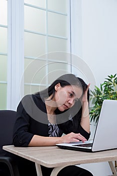 Business woman sitting on chair while holding head in front of laptop