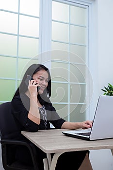 Business woman sitting on chair while making phone call in front of laptop