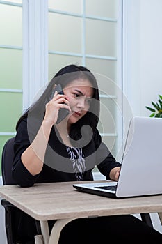 Business woman sitting on chair while making phone call in front of laptop with confused facial expression