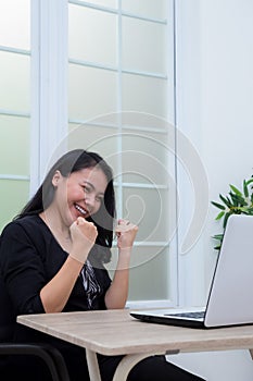 Business woman sitting on chair while raising both hands with success expression in front of laptop