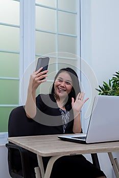 Business woman sitting on chair while waving to cell phone in front of laptop
