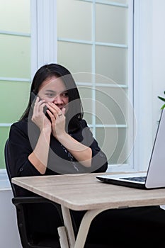 Business woman sitting on a chair while whispering on the phone in front of a laptop