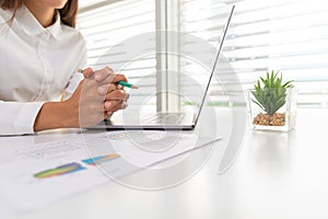 A business woman sitting on a desk with a laptop and graph with gestures in the office Concept .Take a break from the computer.And