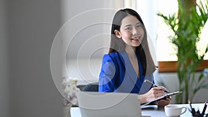 Business woman sitting in front of laptop computer at office desk and smiling at camera.