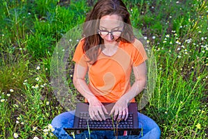 Business woman sitting with laptop in the park, free space.