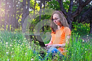 Business woman sitting with laptop in the park, free space.