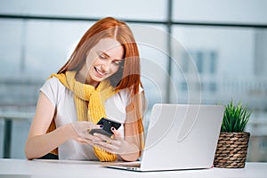 Business woman sitting in office, looking at graphics and uses smartphone