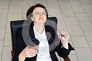 Business woman sitting relaxed on a chair leaning back with closed eyes during coffee break