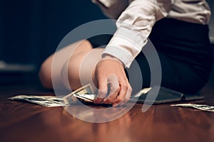 Business woman sitting on table with pile of dollar bills.