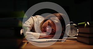 Business woman sleeping at table with alarm clock with documents in office late at night during thunderstorm