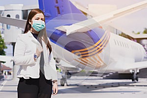 The business woman smiling and wearing protection face mask against coronavirus, PM 2.5 and cold stnding in front of airplane.