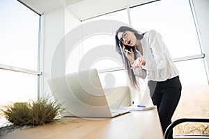 Business woman speak phone and look at laptop in her office.