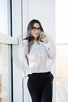 Business woman speak on phone near big office windows