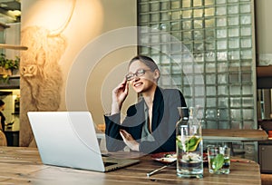 Business woman in spectacles sitting at her desk in cafe and laughing. Woman sitting in cafe with laptop computer on her desk