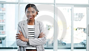 Business woman standing with arms crossed, looking proud and confident in an office alone at work. Portrait of a young