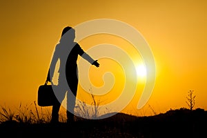 Business woman standing and holding bag at sunset silhouette.