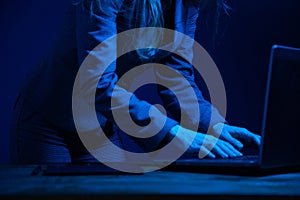 Business woman standing working on a laptop in the dark and illuminated by the screen. No face. Focus on hands. Blue