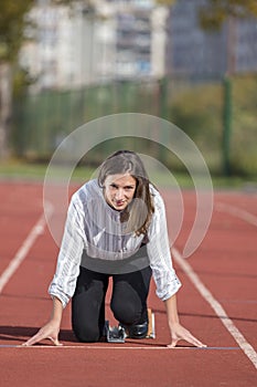 Business woman in start position ready to run and sprint on athletics racing track