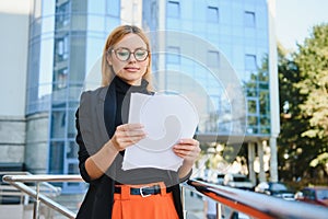 Business woman on the street is looking at a document. Scrolls a folder near the building